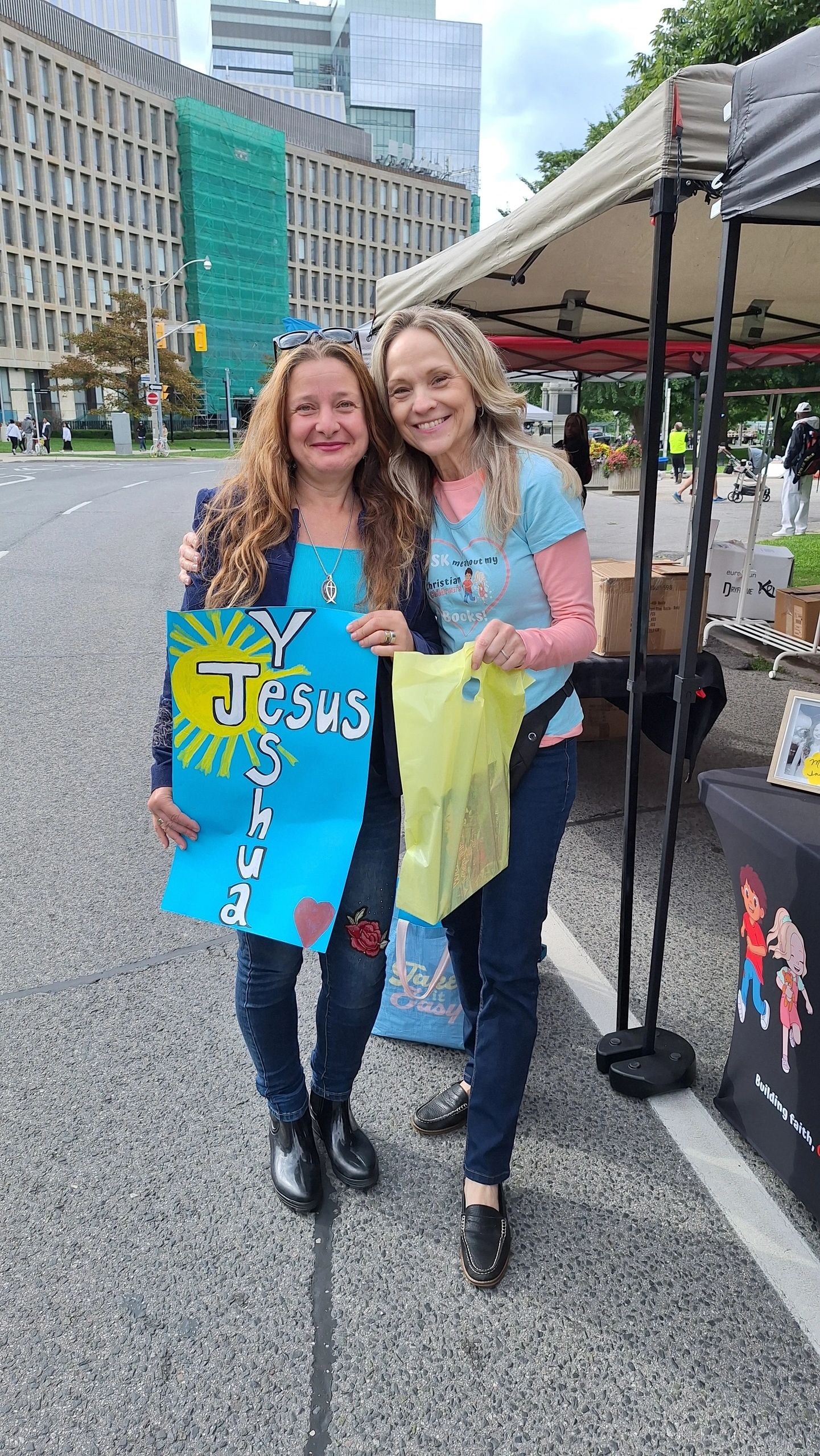 Joanne and a happy customer holding a Yeshua sign at Jesus in the City Parade 2025
