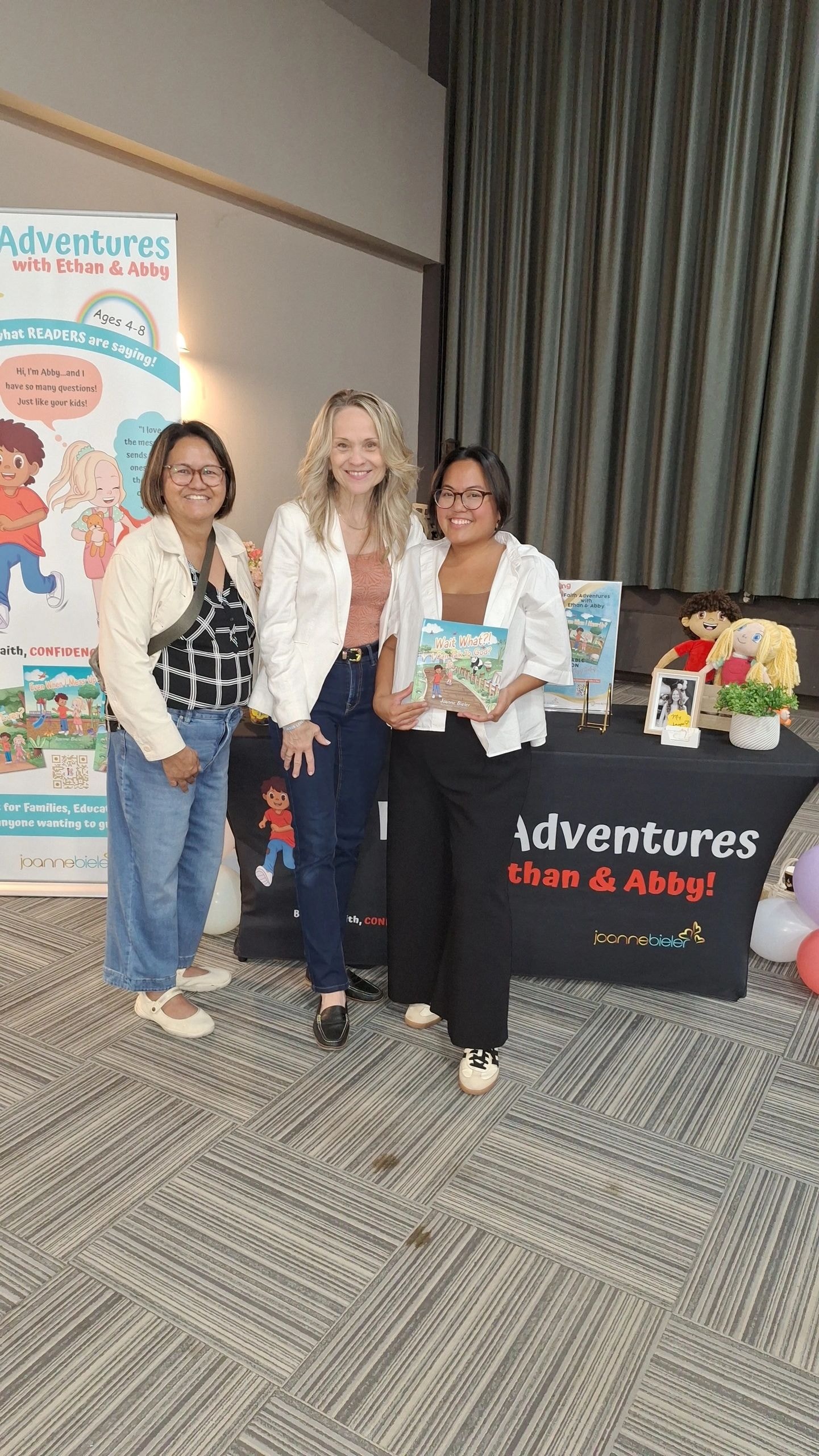 Joanne with Pastor Marivic and Jesse Magallano at Jesus Is Alive Community event book table