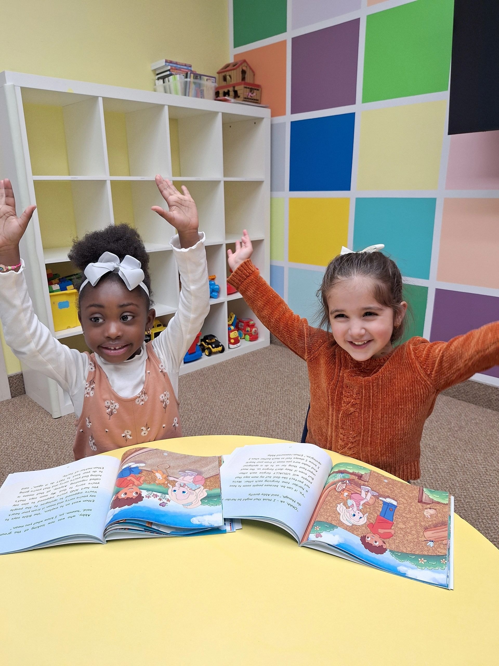 Lavignia and Leila with arms raised celebrating with Faith Adventures books open on the table