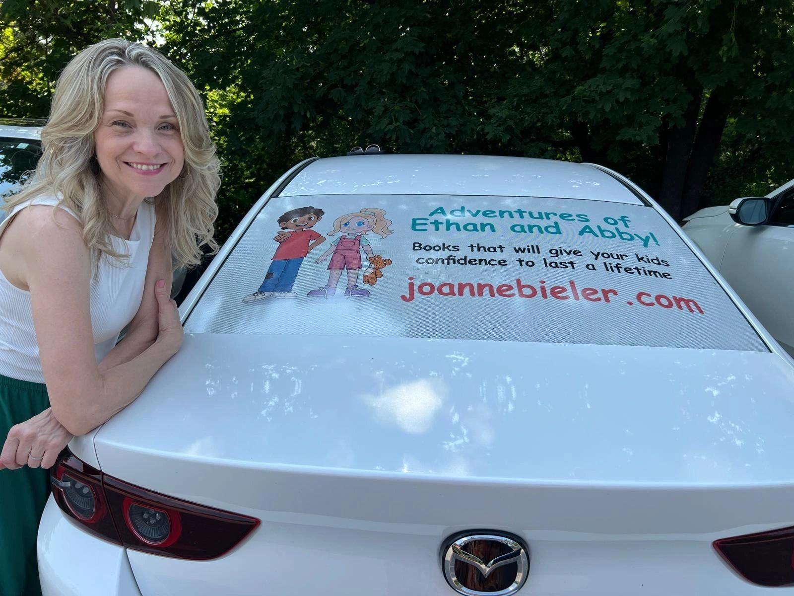 Joanne leaning on her car with Adventures of Ethan and Abby sunshade at Women of Excellence Conference Toronto