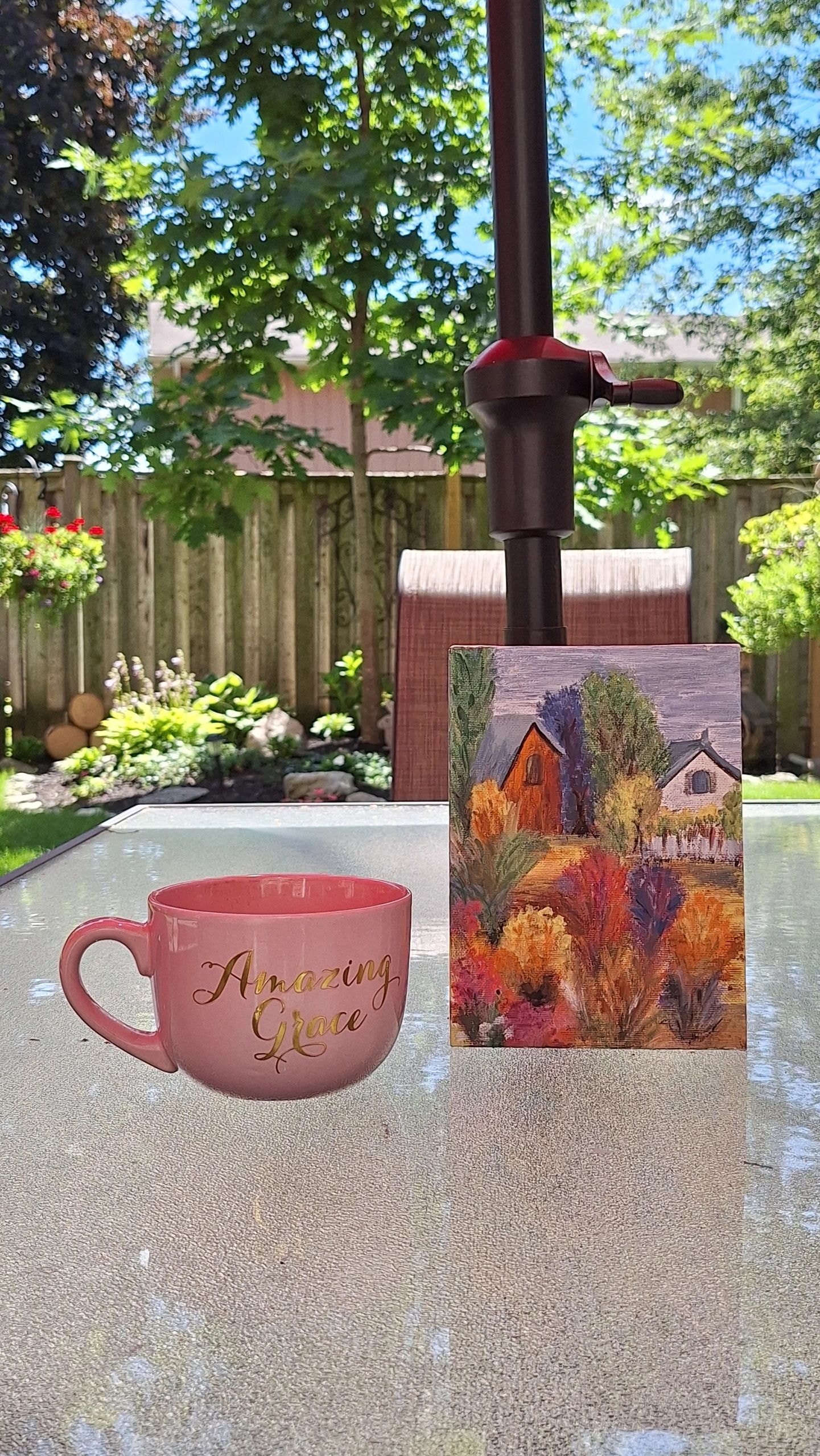 Amazing Grace mug beside a small landscape painting on a backyard patio table