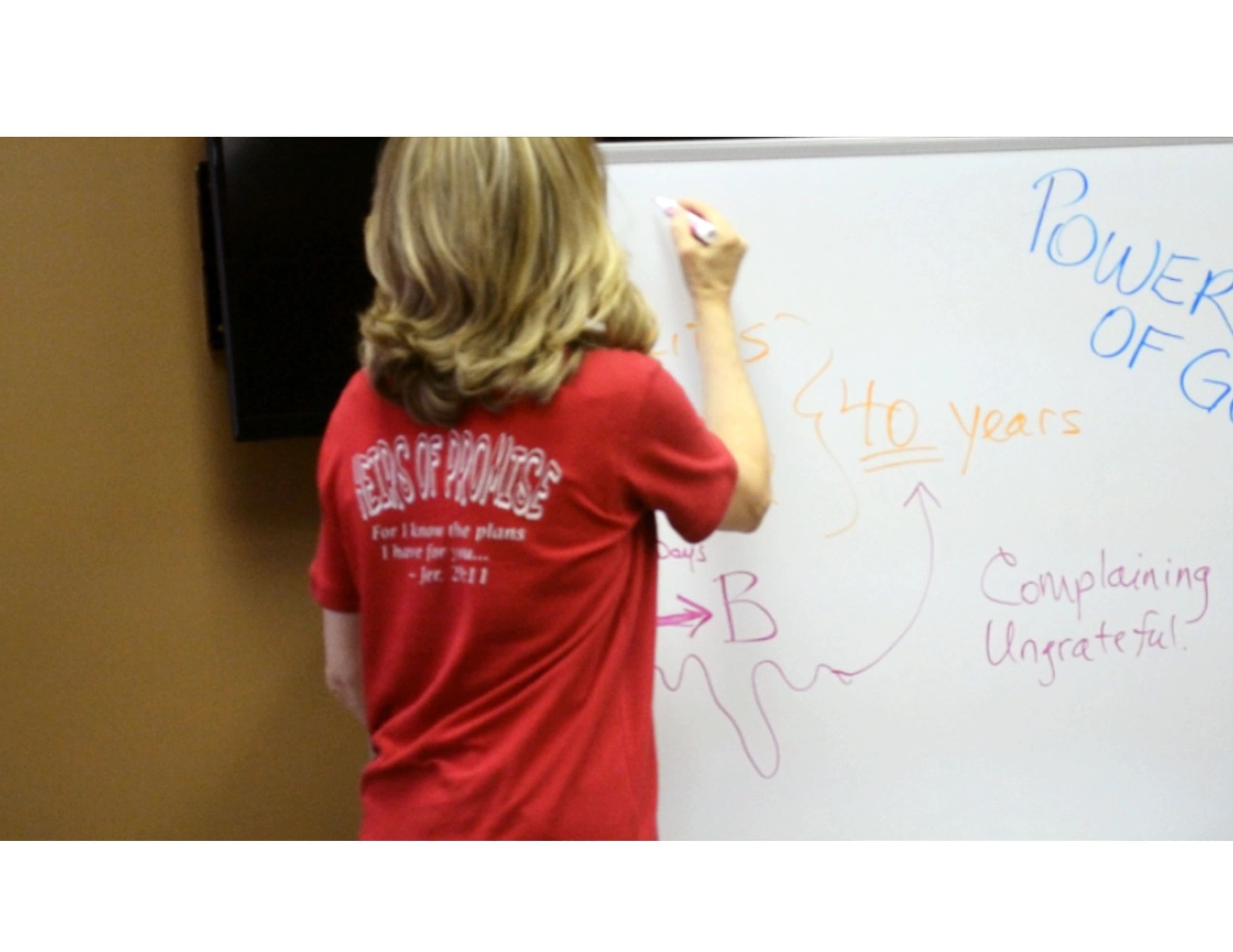 Joanne teaching children at whiteboard about the Power of God wearing a Kids of Promise t-shirt
