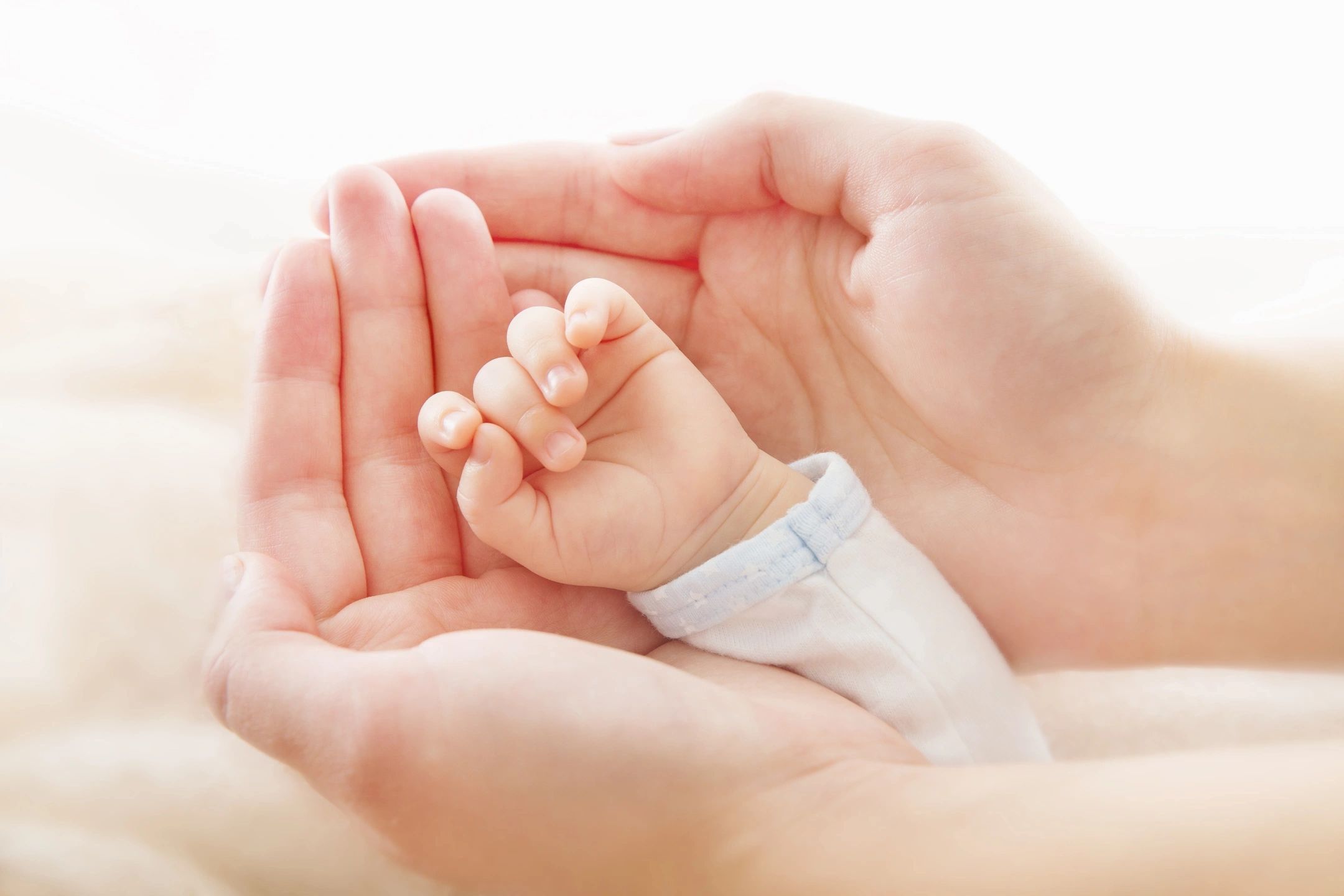 A tender moment — adult hands cradling a newborn